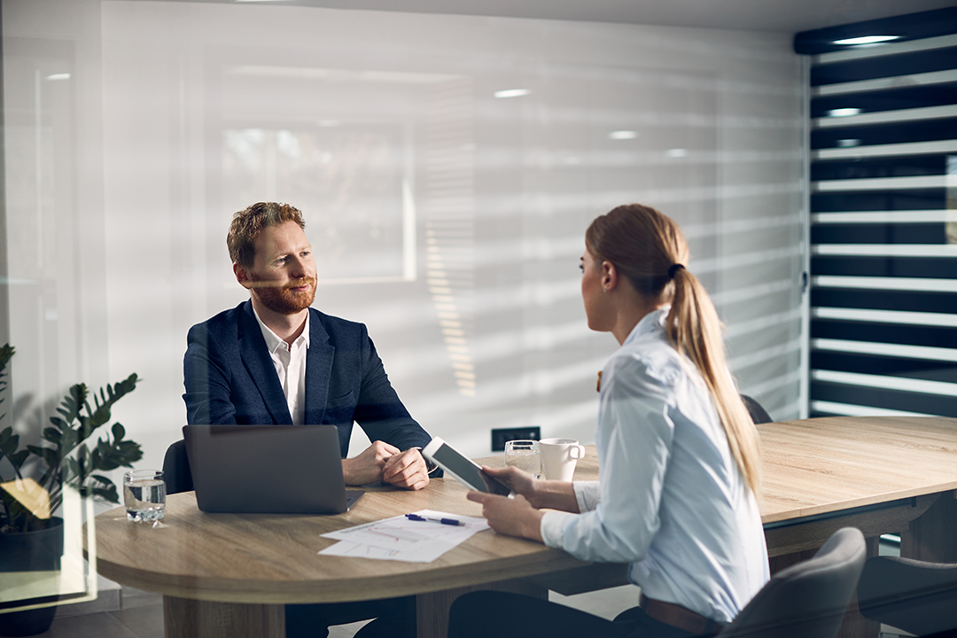 Two business coworkers communicating while having a meeting in the office. The view is through the glass.