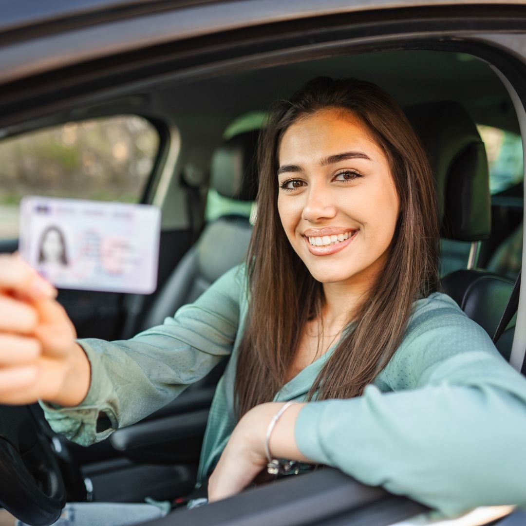 teenager sitting in driver's seat holding an ID