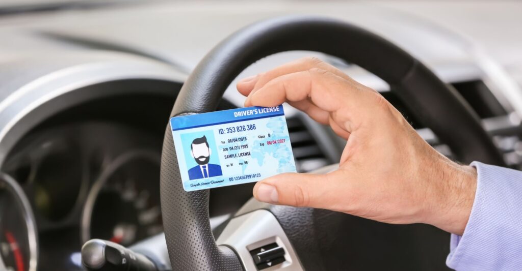 Person holding a mock drivers license in front of a steering wheel.