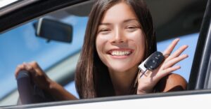 smiling teenager sitting in car with car keys