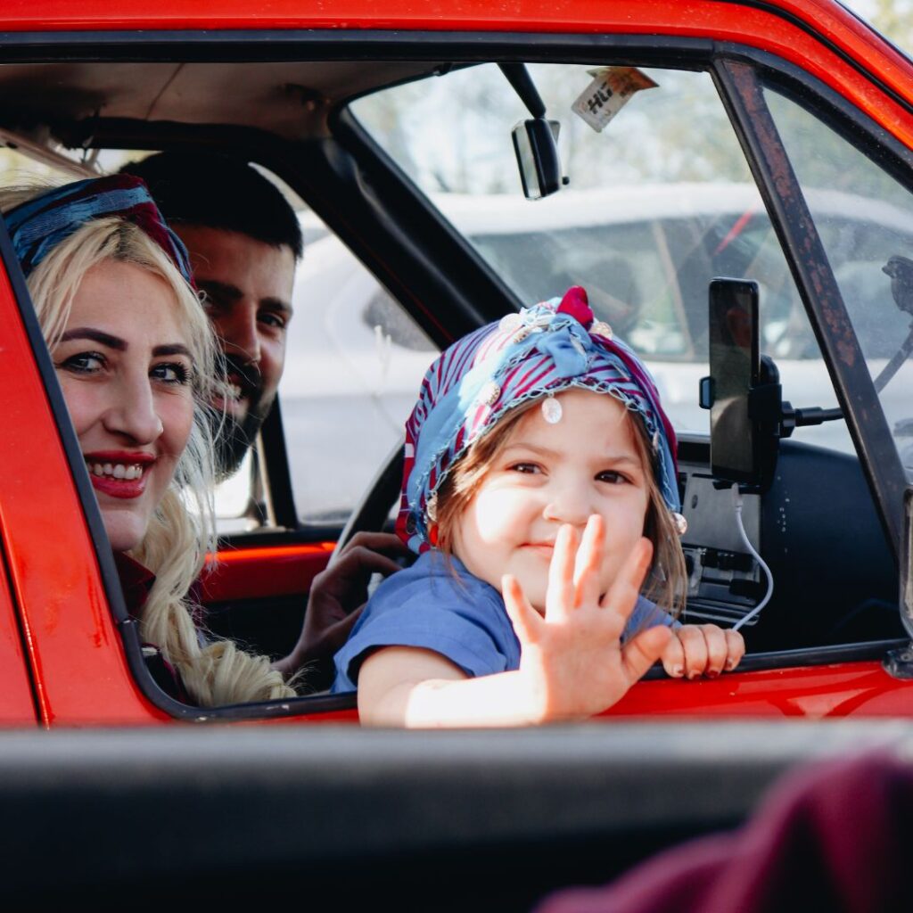 Family smiling and waving from inside their car